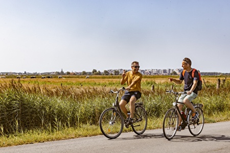 twee mannen in zomerse kledij fietsen door de velden met skyline van Blankenberge in de verte