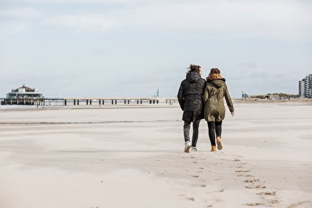 Koppel in winterse kledij loopt over het strand richting Pier