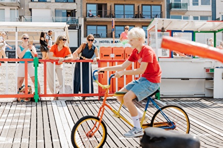 kind op gekke fiets terwijl dames staan toe te kijken